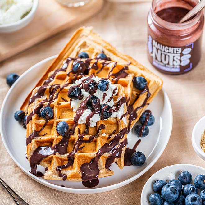 Waffeln mit Blaubeeren, Schlagsahne und Schokoladensauce auf einem Teller